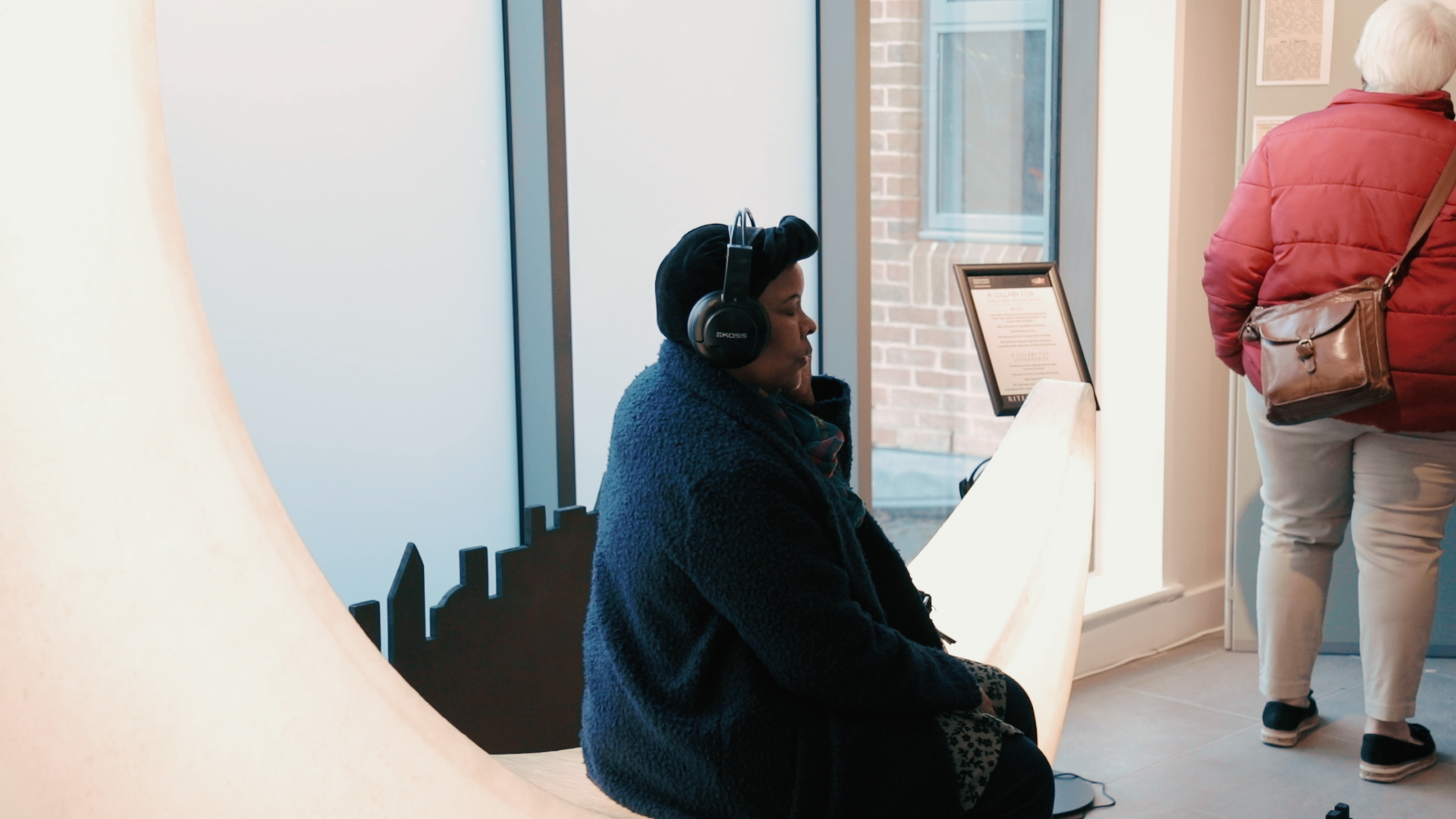 An audience member who is wearing headphones, sits on a large crescent moon prop and listens to the recording.